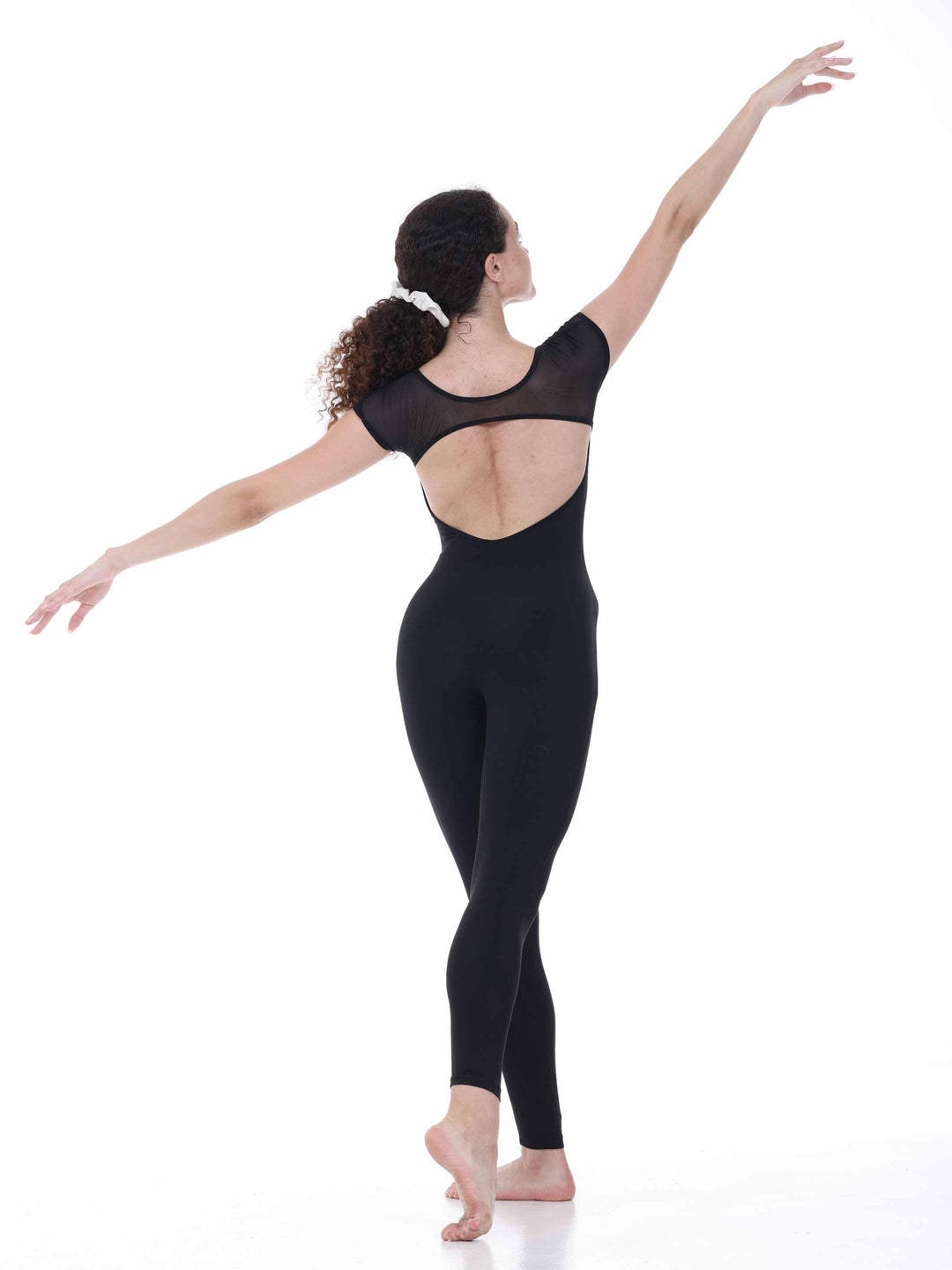Danseuse vue de dos portant la unitard de danse Sway – modèle Sheer Cap Sleeve Dance Unitard en negro, bras étendus dans une posture gracieuse, sur fond blanco.