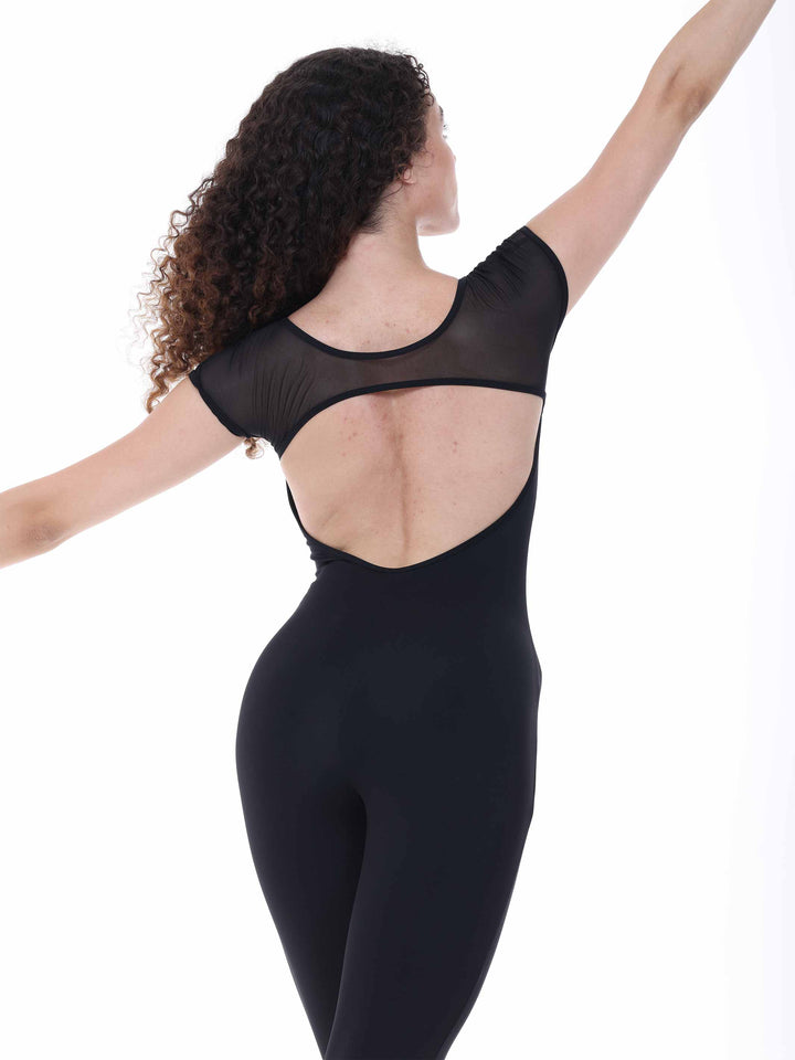 Danseuse portant la unitard Sway – modèle Sheer Cap Sleeve Dance Unitard en negro, levant gracieusement un bras en pose de ballet, sur fond blanco.