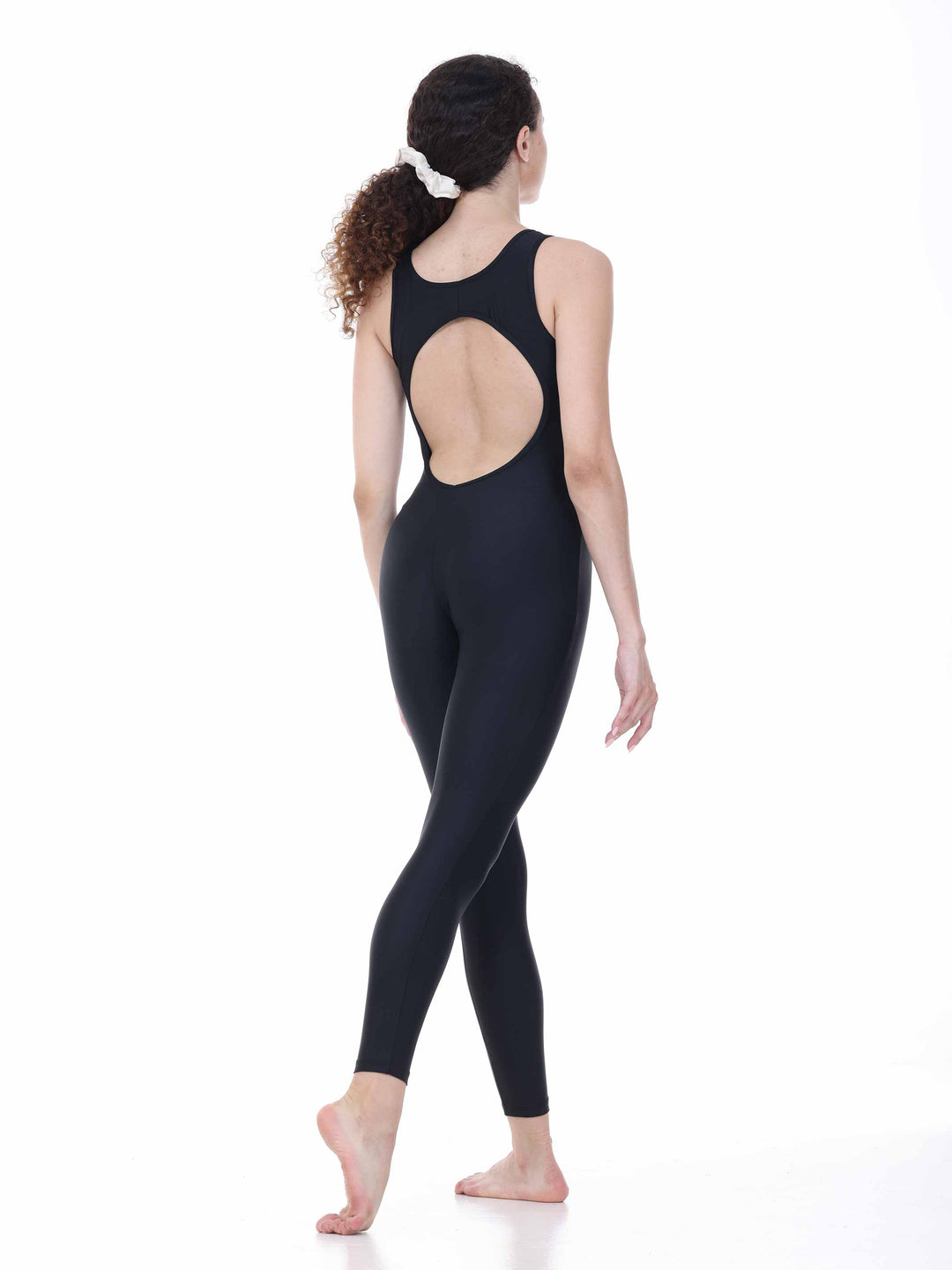Danseuse vue de dos portant un maillots intégral negro à dos rond ajouré, en position de marche gracieuse sur fond blanco.