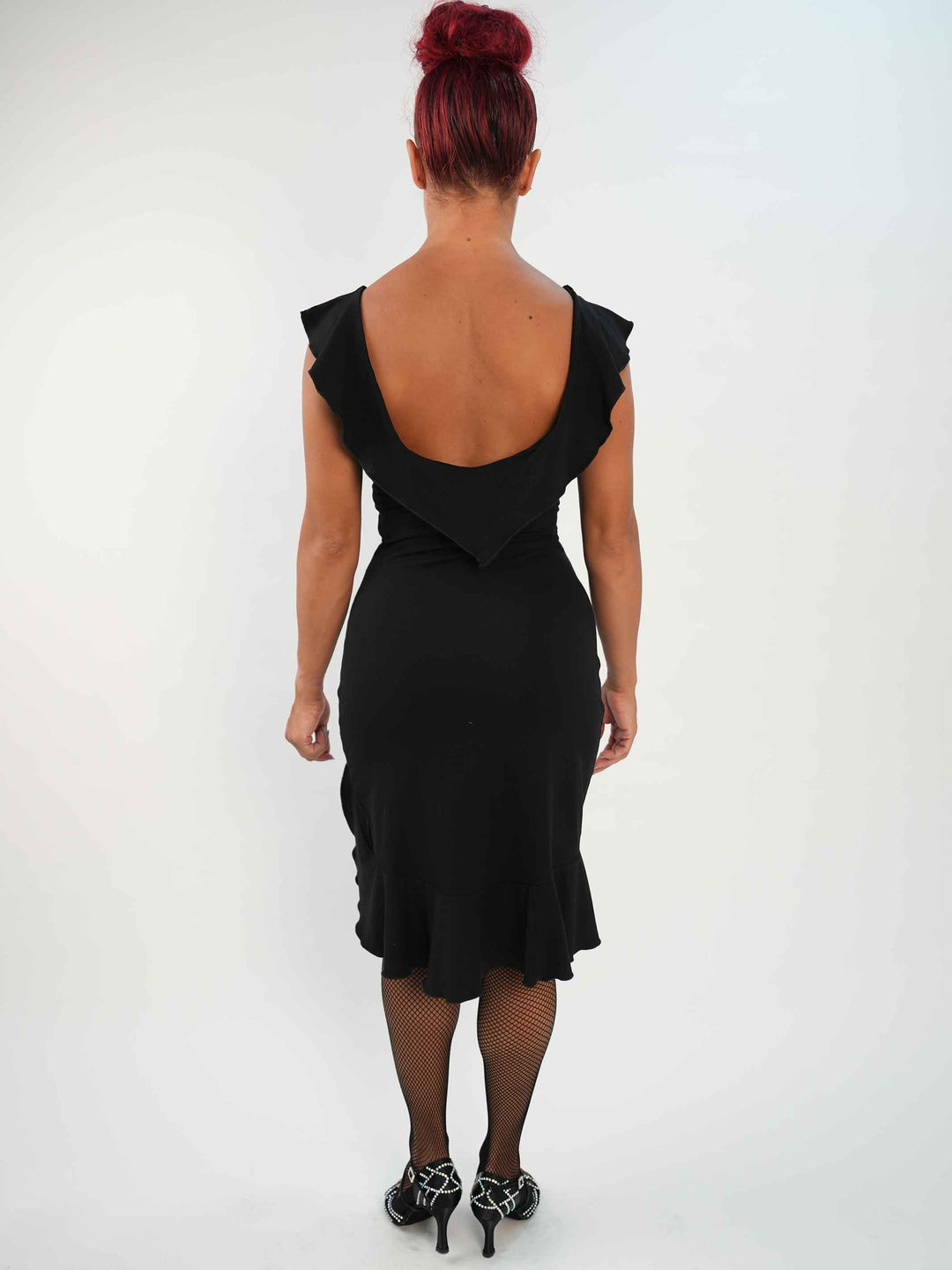 Femme portant une robe noire de danse latine sans manches, avec encolure volantée et ourlet asymétrique, associée à des collants résille et des chaussures de danse ornées. Tenue élégante et fluide, parfaite pour la salsa ou le ballroom. - vue de l&