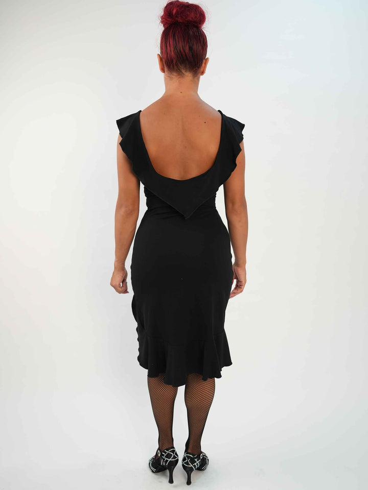 Femme portant une robe noire de danse latine sans manches, avec encolure volantée et ourlet asymétrique, associée à des collants résille et des chaussures de danse ornées. Tenue élégante et fluide, parfaite pour la salsa ou le ballroom. - vue de l&